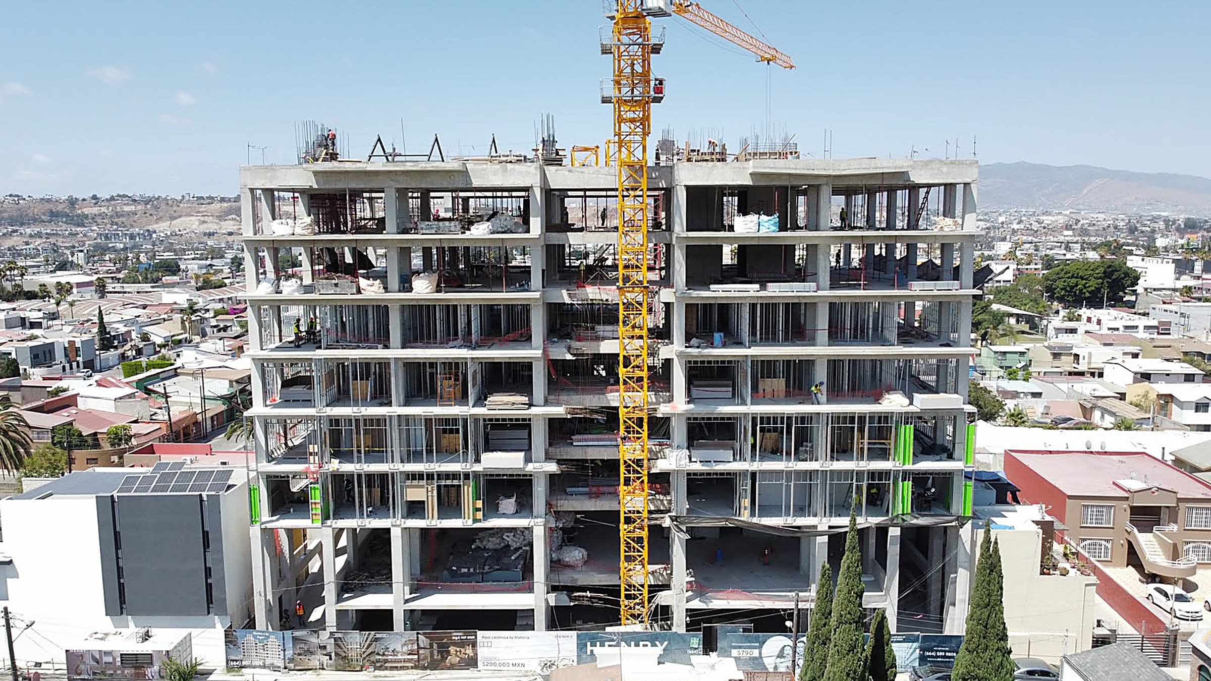 Vuelo de dron sobre Henry en La Ermita — el edificio en obra con Tijuana y los cerros detrás, fotografía aérea